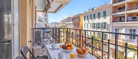 A balcony with a table set for breakfast, including croissants, fruit, and juice.