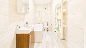 Een moderne badkamer met een wastafel, bad en toilet, met lichte tegels en houten kastjes.