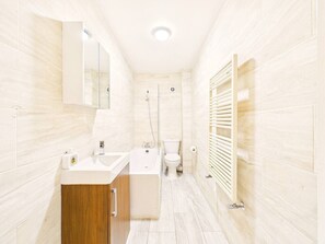 A modern bathroom with a sink, bathtub, and toilet, featuring light-colored tiles and wooden cabinetry. - Stylish Watford Stay | Modern | Sleeps 5 (Hertfordshire)