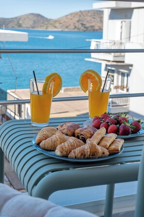 Un balcón con una mesa dispuesta para el desayuno, incluyendo croissants y fresas, y dos vasos de zumo de naranja con rodajas de limón.