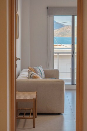 Une chambre moderne avec un canapé, une petite table en bois et une vue sur la mer, visible à travers une grande fenêtre.