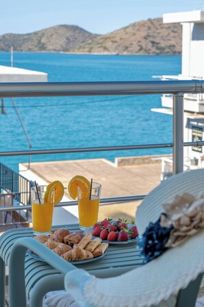 Un balcón con una mesa preparada para el desayuno, con vista a un cuerpo de agua y un paisaje montañoso.