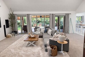 A spacious living room with a grey sofa, a wooden coffee table, and a large window offering a view of the outdoors.