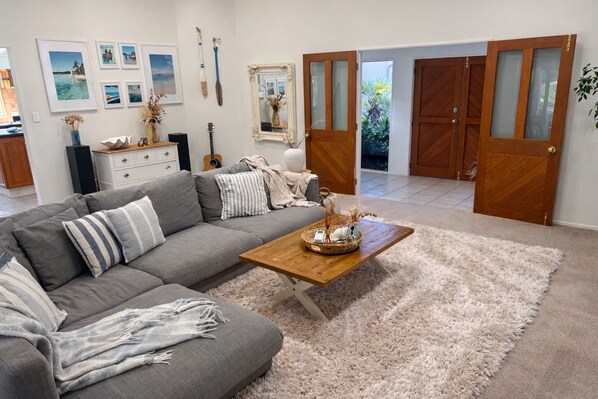 A living room with a grey sectional sofa, a wooden coffee table, a fluffy rug, a guitar, framed photos, and a mirror.
