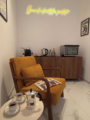 Un coin accueillant avec une chaise en bois, une petite table sur laquelle se trouvent une cafetière et des tasses, un panneau lumineux au néon, une bouilloire et un téléviseur posé sur un meuble en bois.