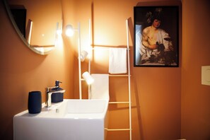 A bathroom with a white sink, a mirror, a towel rack, and a framed painting on the wall. - Vrbo Property (Frascati)