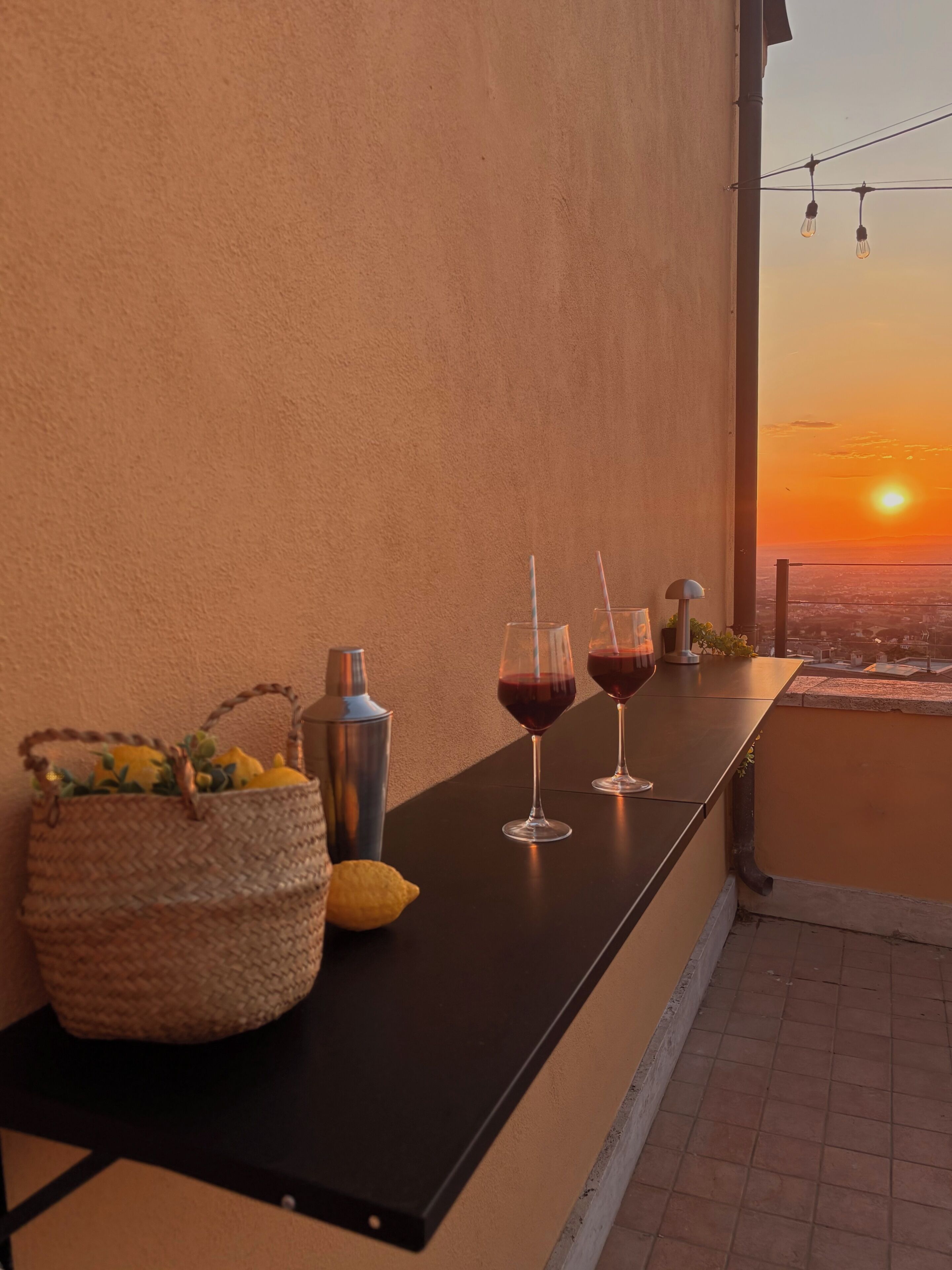 Ein Balkon mit Tisch für zwei Personen, einem Cocktail-Shaker, einer Flasche und einem Korb voller Zitronen.