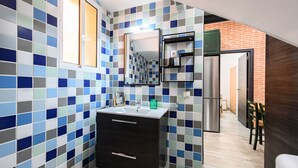 Ein modernes Badezimmer mit gefliestem Spritzschutz, einem Waschbecken, einem Spiegel und einem Edelstahlkühlschrank.