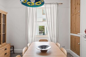 A dining area with a wooden table, white curtains, a stained glass ceiling, and a view through the window. - Beautiful Victorian Home, Garden & Patio, Torquay (Torquay)