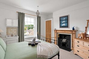 A bedroom with a bed, a fireplace, a window with curtains, a wooden dresser, and a framed picture on the wall. - Beautiful Victorian Home, Garden & Patio, Torquay (Torquay)