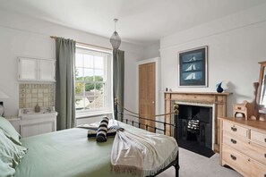 Ein Schlafzimmer mit Bett, Fenster, Kamin, Spiegel und Schrank.