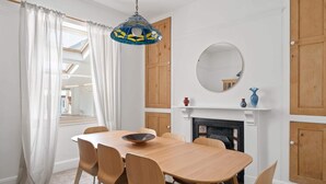 En spisestue med et træbord, stole, en hængende lampe, en pejs og et spejl på væggen.