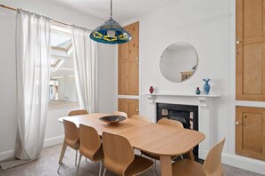 Ein Esszimmer mit Holztisch und Stühlen, einer Hängelampe, einem Kamin und einem Spiegel an der Wand.