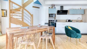 Eine moderne Küche mit einer Holztreppe, einem Esstisch mit Stühlen und einem sesselartigen Sessel in Türkis.