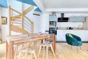 Eine moderne Küche mit einer Holztreppe, einem Esstisch mit Stühlen und einem sesselartigen Sessel in Türkis.