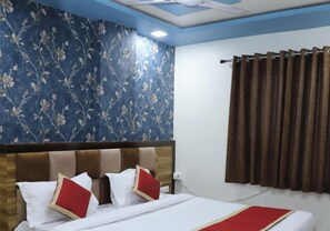 Een hotelkamer met een bed, hoofdeinde, raam met gordijnen en een bloemen behang.