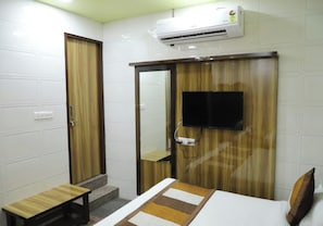 A hotel room with a bed, a wooden bench, a TV mounted on the wall, and an air conditioning unit. - Hotel Sheeba Ajmer (Ajmer)