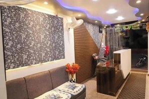 A reception area with a sofa, a vase with flowers, a wooden panel wall, and a motorcycle in the background. - Hotel Sheeba Ajmer (Ajmer)