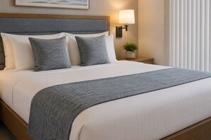Ein ordentlich bezogenes Bett mit grauer Decke, ein grauer Rahmen an der Kopfteil und eine Nachttischlampe.