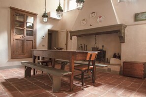 Een rustieke eetruimte met een houten tafel, banken en een open haard.