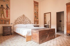 Una camera da letto con un letto, un baule di legno, comodini, uno specchio e decorazioni murali egiziane.