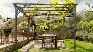 Un giardino con una pergola, un tavolo e sedie, e un muro in pietra.