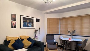 Een woonkamer met een donkergroene bank, een klein tafeltje en een eethoek met stoelen.