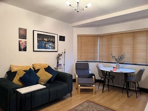 Ein Wohnzimmer mit einem dunkelgrünen Sofa, einem kleinen Tisch und einem Essbereich mit Stühlen.