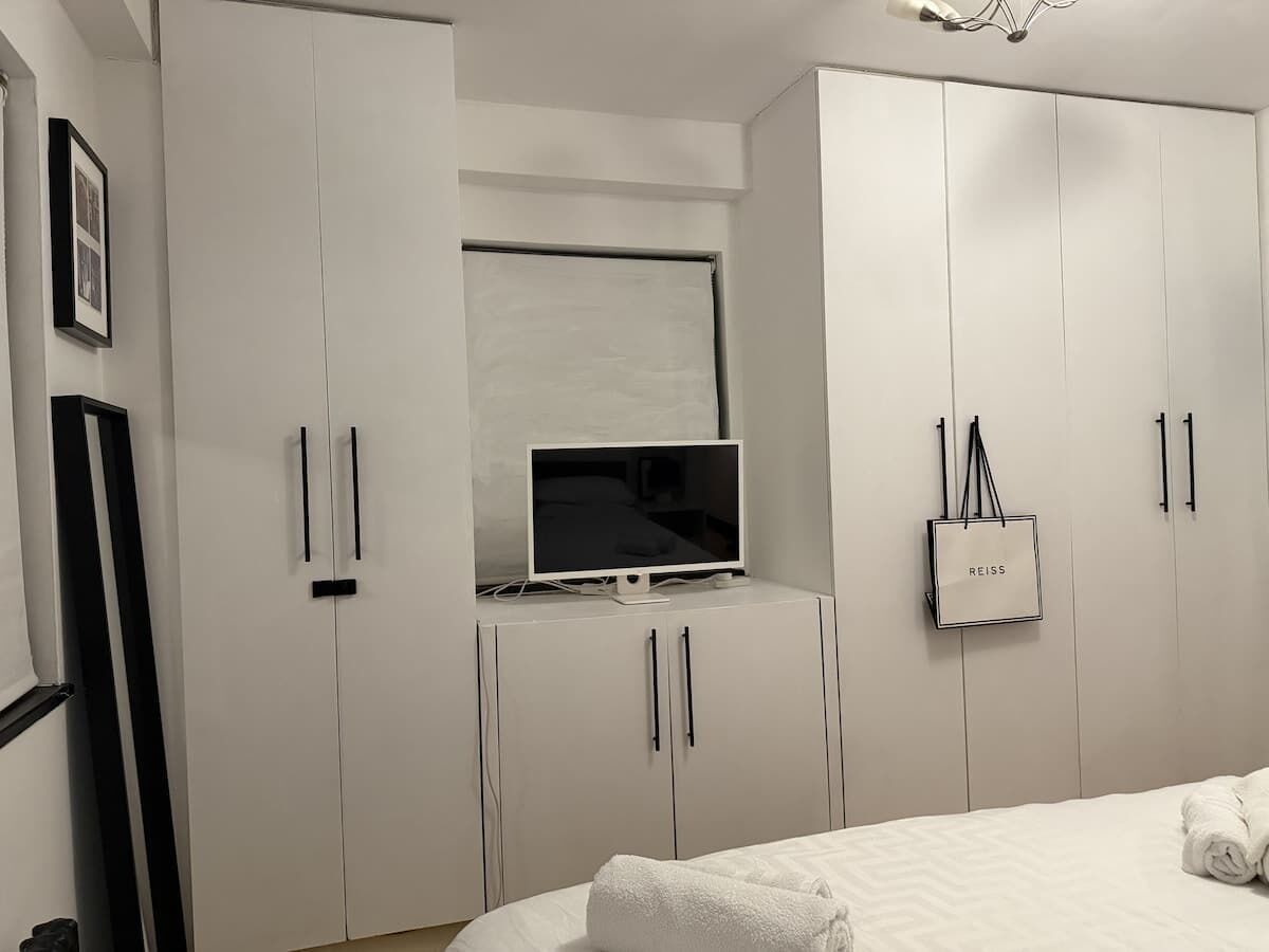Ein Schlafzimmer mit Bett, Fernseher auf einem Schrank, einem Kleiderschrank und einer REISS Tasche.
