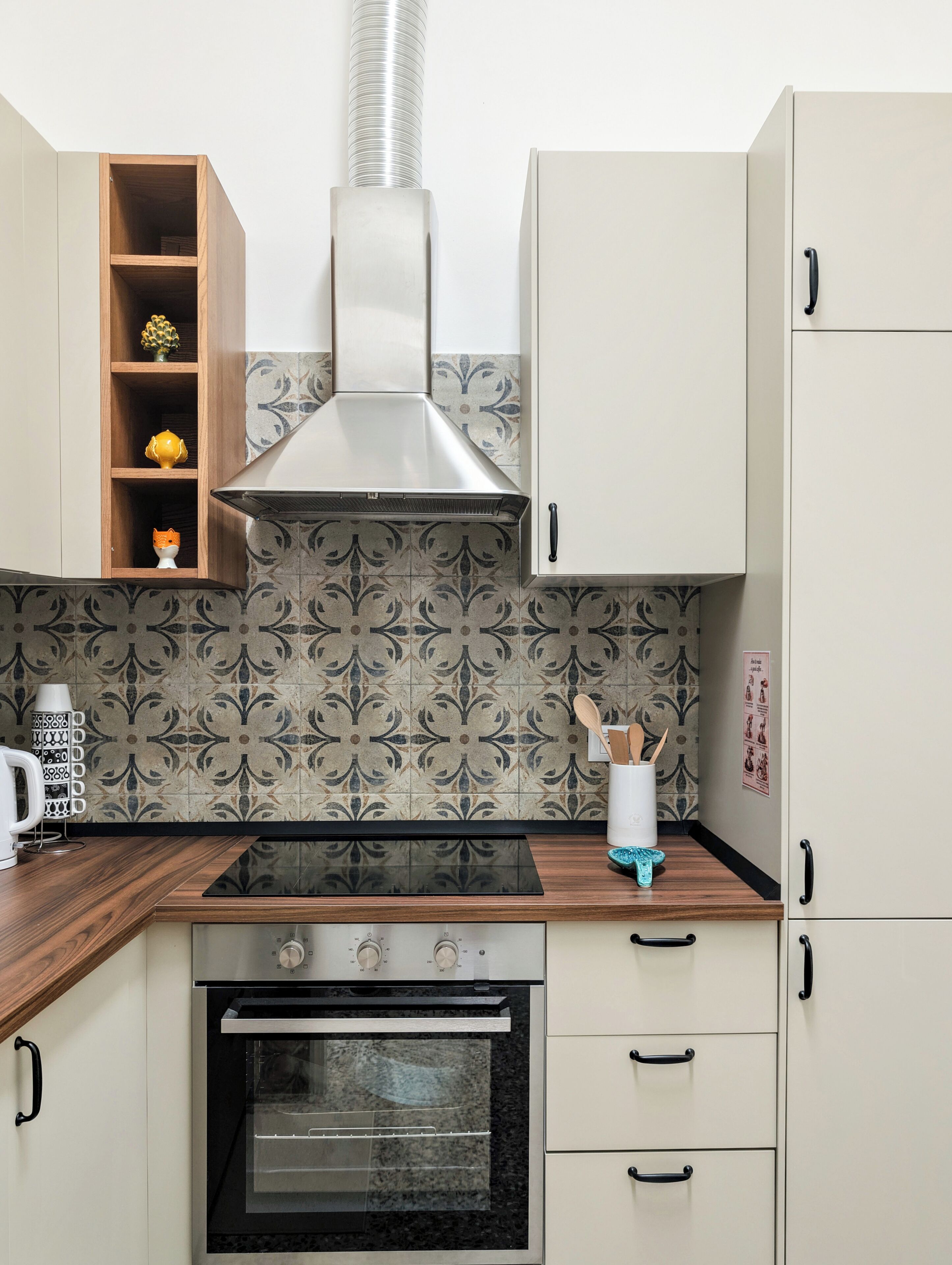 Una cucina con fornello, forno, mensole in legno e zoccolo paraschizzi decorato.