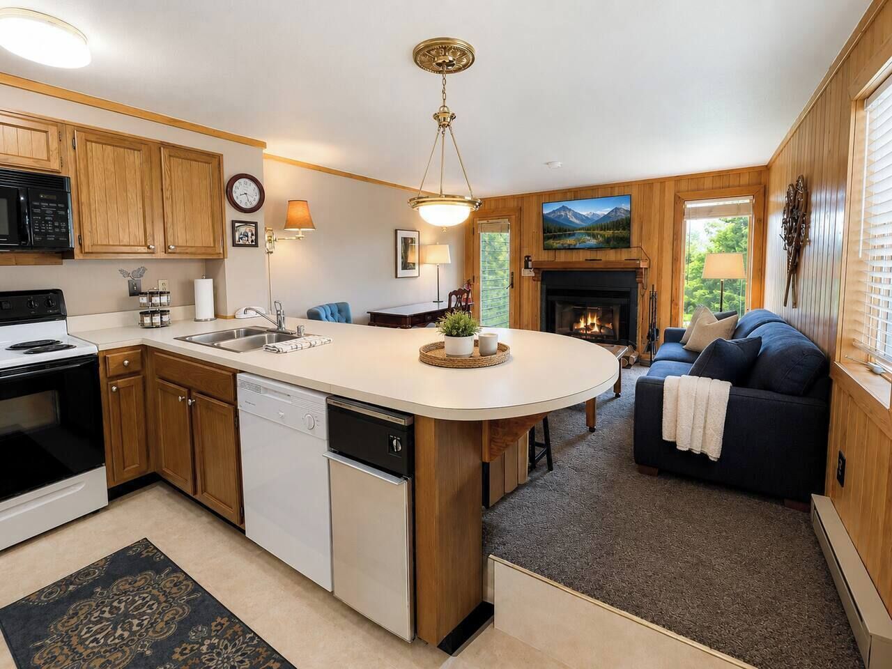 A compact kitchen with wooden cabinets, a built-in dishwasher, a central island, and a fireplace.