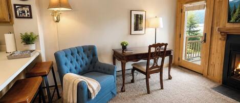 A cozy room with a blue sofa, wooden dining table, chairs, a lamp, a clock, and a fireplace.