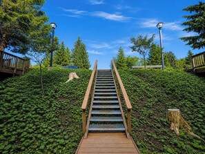 Eine Holztreppe führt einen Hügel hinauf, umgeben von Grünpflanzen und Bäumen.