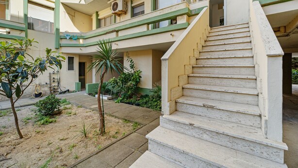 Ein mehrstöckiges Gebäude mit einer zentralen Treppe, Außenpflanzen und einer sichtbaren Klimaanlage.