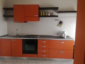 Eine Küche mit orangenen Schränken, einem Gasherd, einem Geschirrspüler und einer weißen Fliesenrückwand.