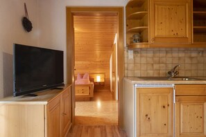 A wooden interior with a TV on a cabinet, a kitchen area with a sink, and a hallway leading to a bedroom with a window. - Quiet and charming apartment with a beautiful view (Schruns-Tschagguns)