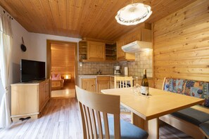 A cozy cabin-style room with a wooden ceiling, a dining table with chairs, a sofa, a television, and a kitchenette. - Quiet and charming apartment with a beautiful view (Schruns-Tschagguns)