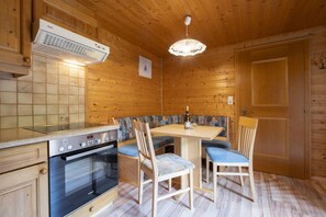 A wooden cabin interior with a kitchen area featuring a stove, a dining table with chairs, and a bench. - Quiet and charming apartment with a beautiful view (Schruns-Tschagguns)
