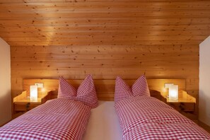 A double bed with checkered bedding, two bedside tables with lamps, and a wooden ceiling. - Quiet and charming apartment with a beautiful view (Schruns-Tschagguns)