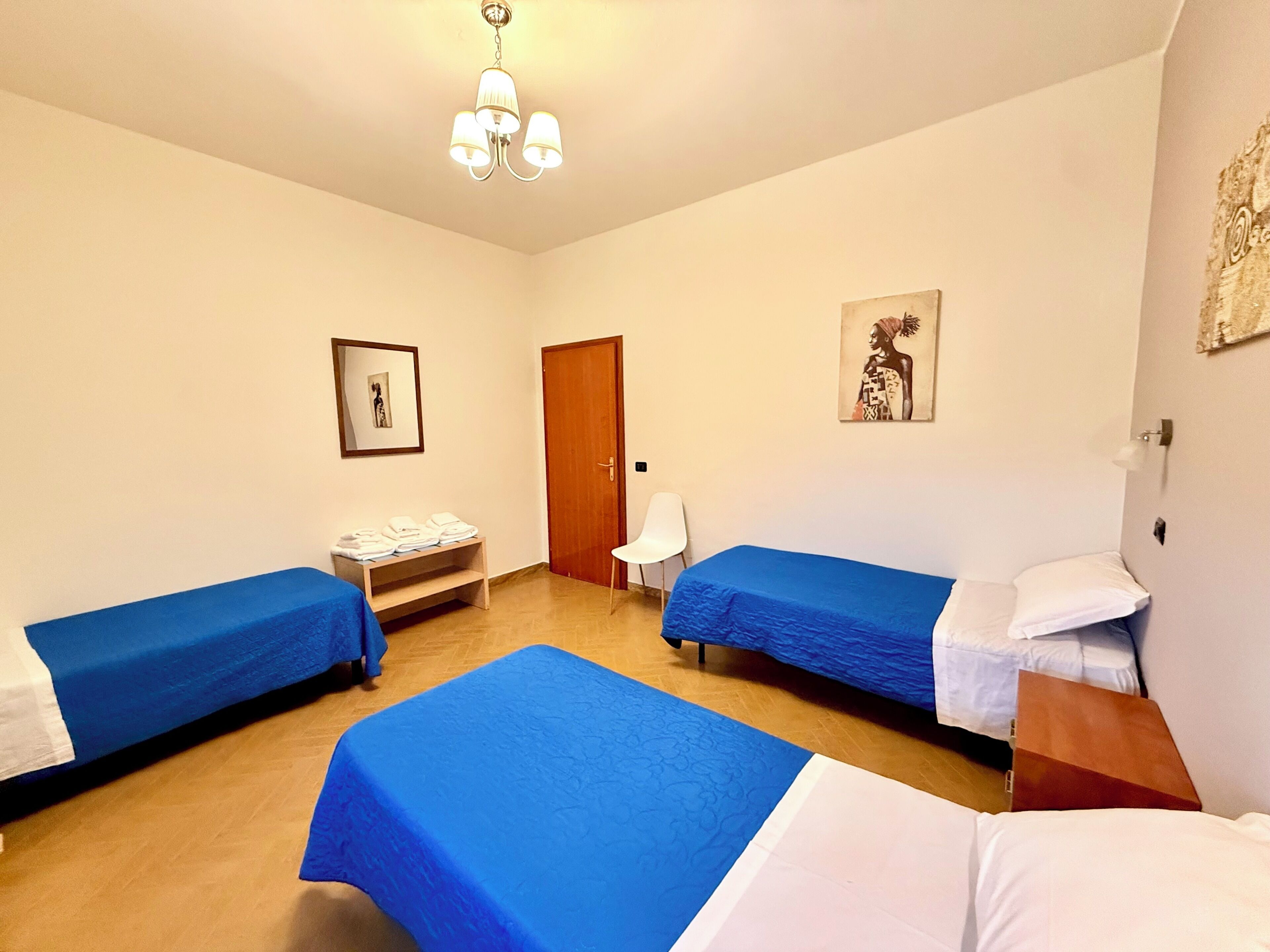 Habitación de hotel con dos camas, un banco de madera, una silla, una puerta y una lámpara en el techo.