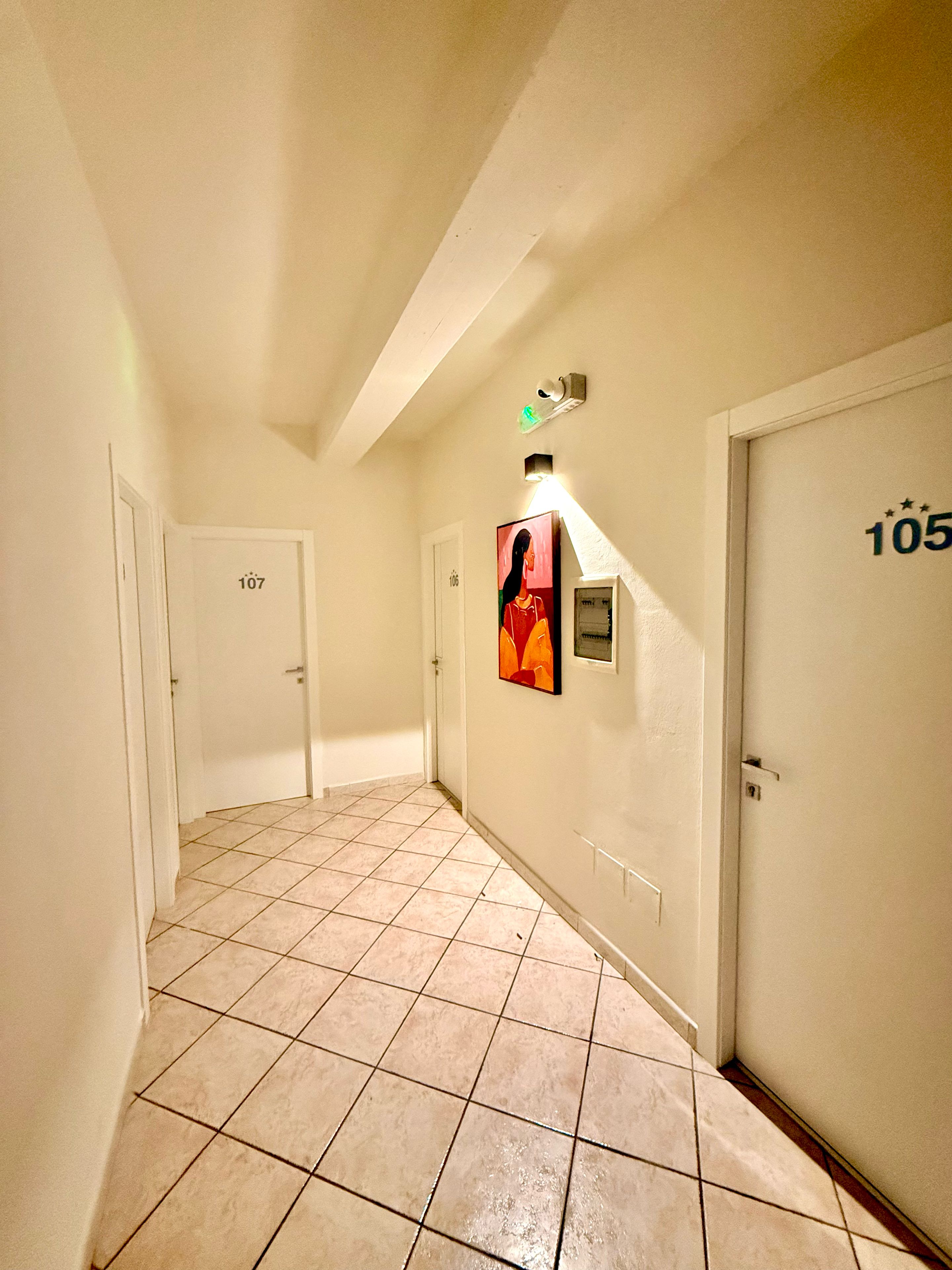 En hall med kakelgolv, dörrar numrerade 105 och 107 samt en väggmonterad lampa.
