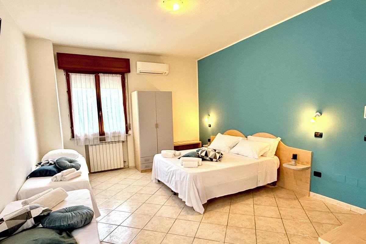 Un dormitorio con cama, mesita de noche, armario, radiador y ventana con cortinas.