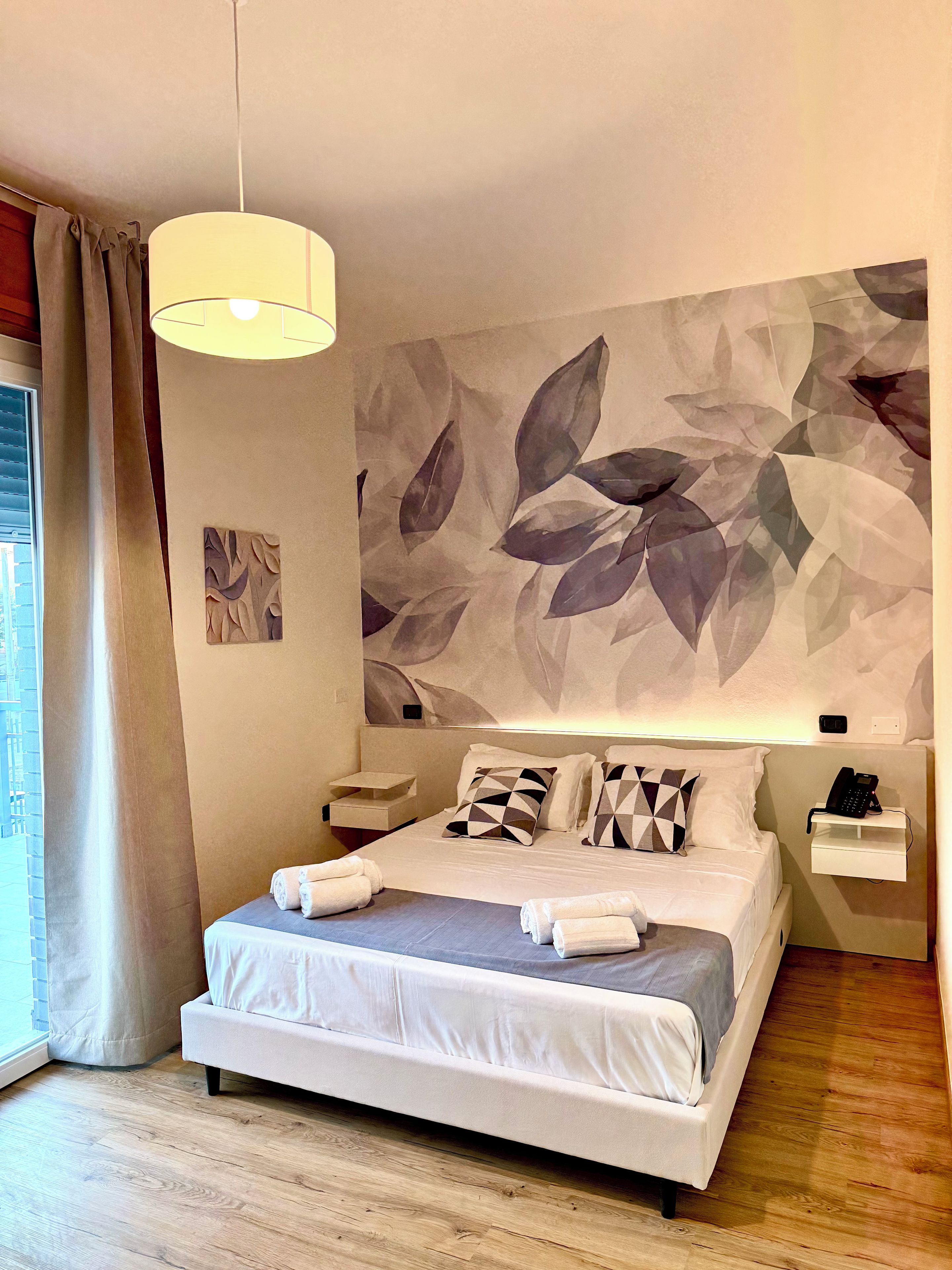A modern hotel room with a large bed, a bedside table, a wall-mounted phone, and a window with curtains.