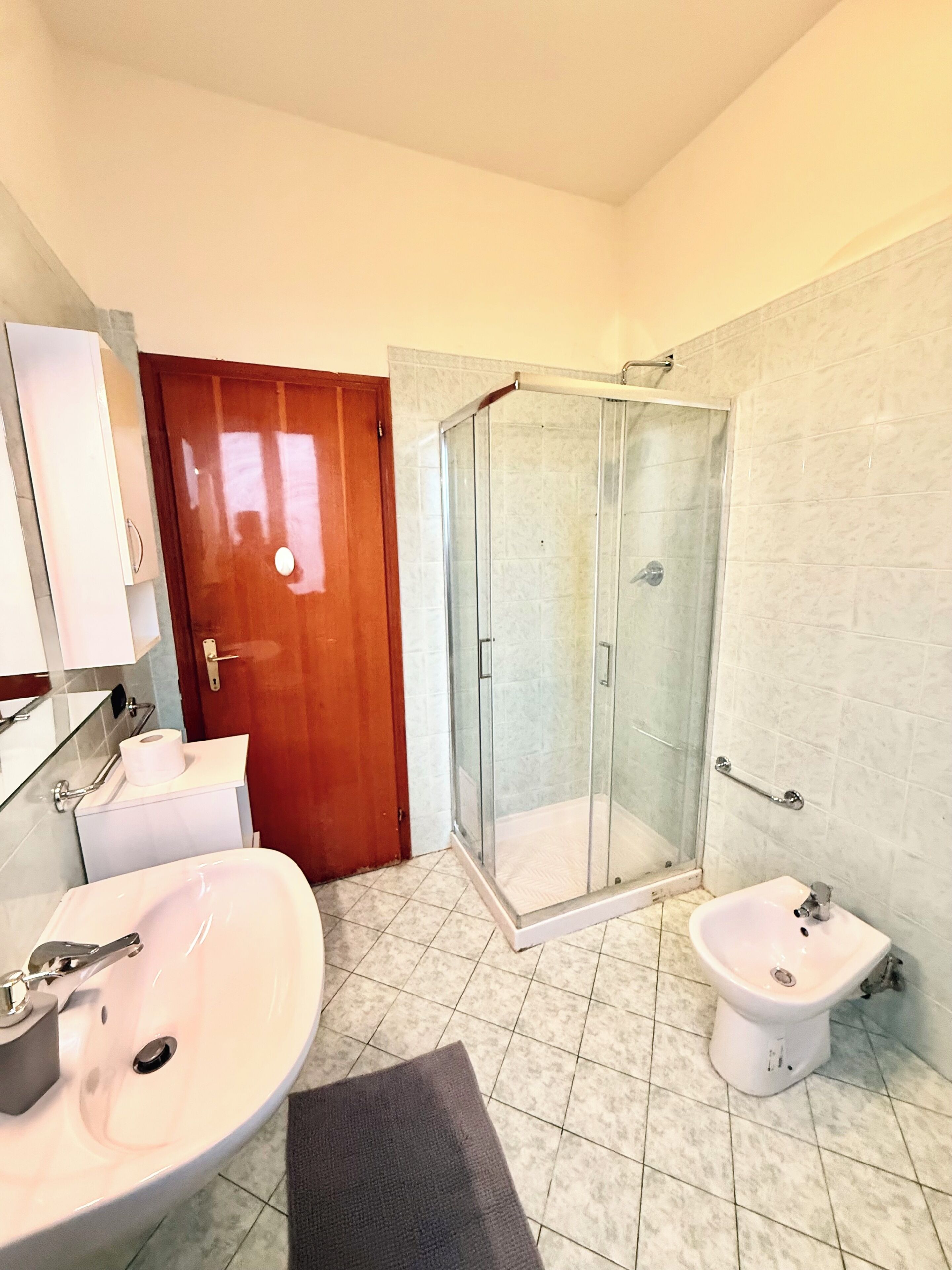 Un baño con ducha, dos lavamanos, inodoro y espejo.