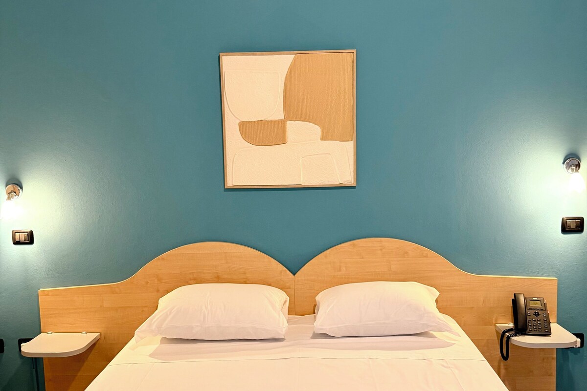 A hotel room with a large bed, two bedside tables, a wall-mounted phone, and a painting.