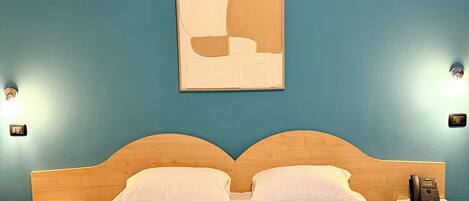 A hotel room with a bed, two bedside tables, a wall-mounted phone, and a painting.