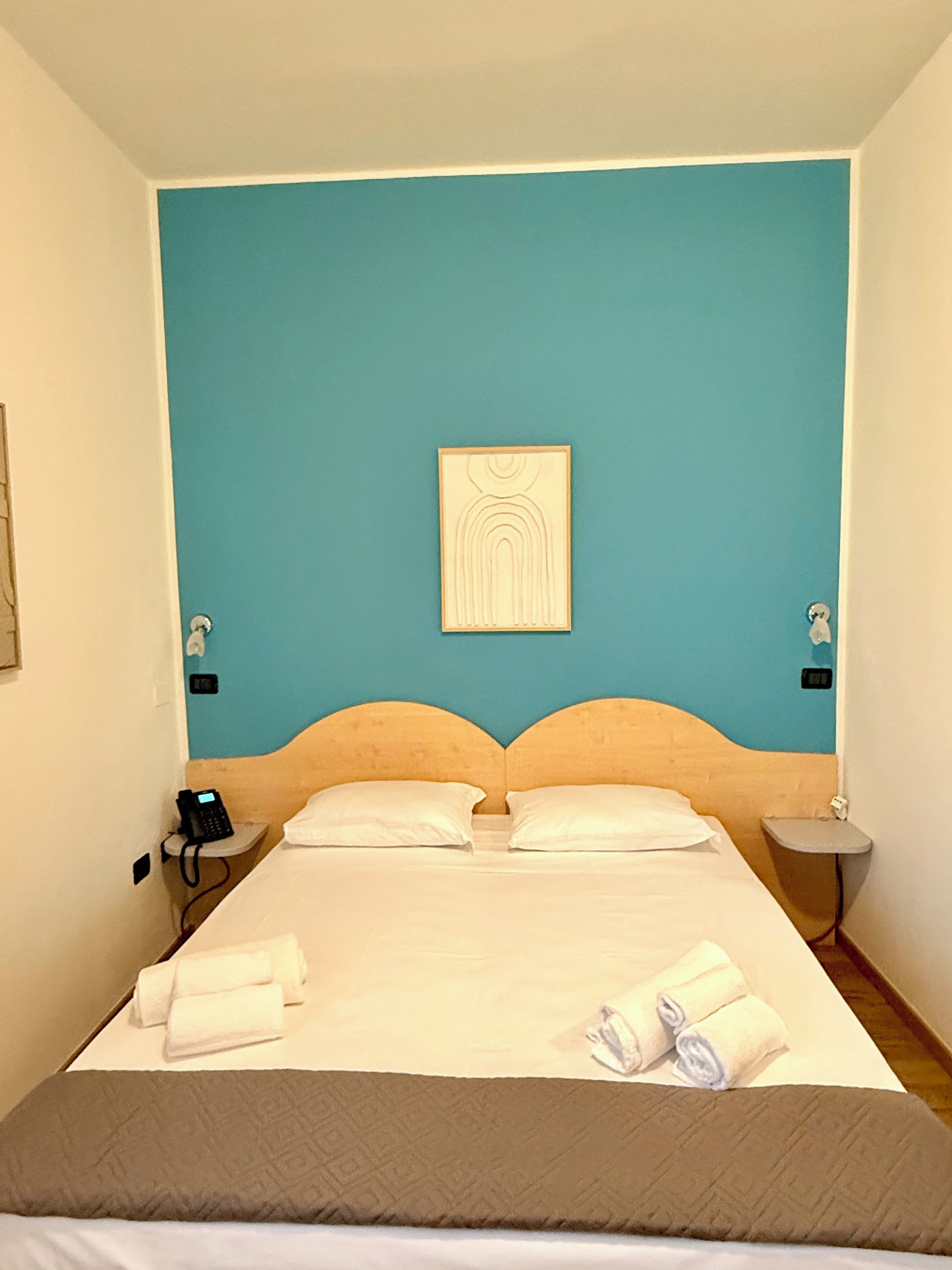 A hotel room with a single bed, two bedside tables, a wall-mounted artwork, and a telephone on the left table.