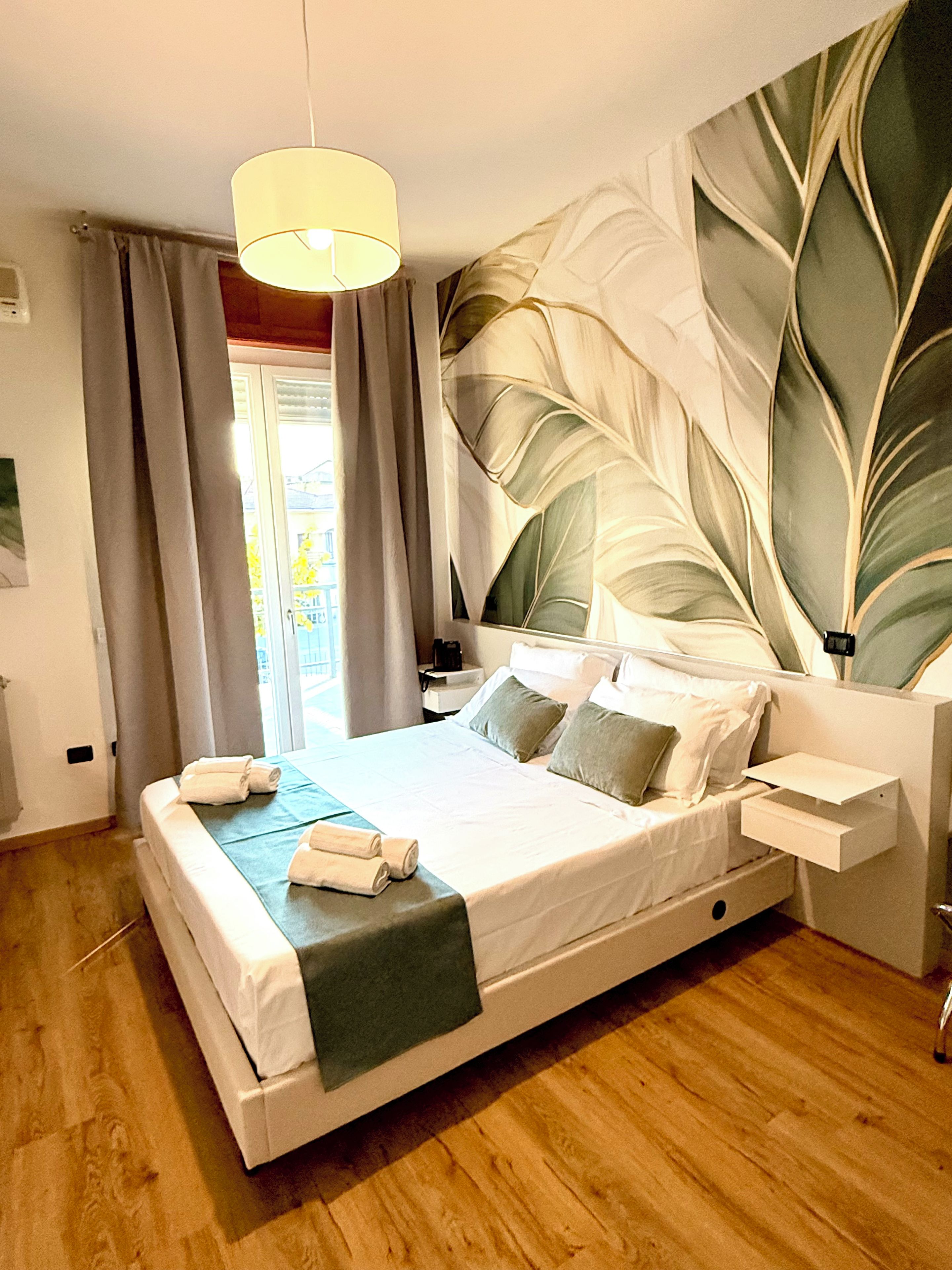 A hotel room with a large bed, a nightstand, a lamp, and a view of the outdoors.