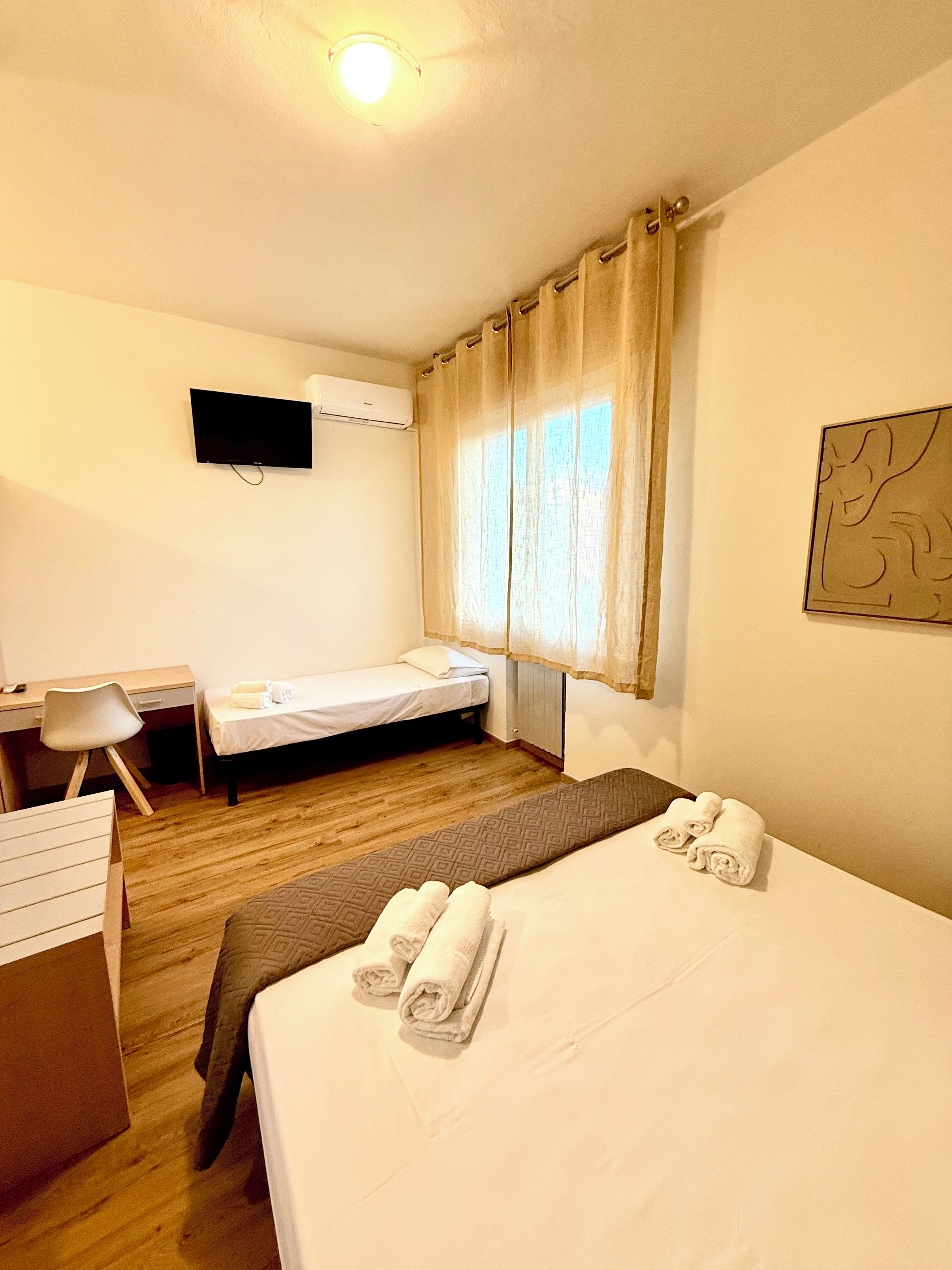 A hotel room with a bed, a desk, a chair, a TV, and a window with curtains.
