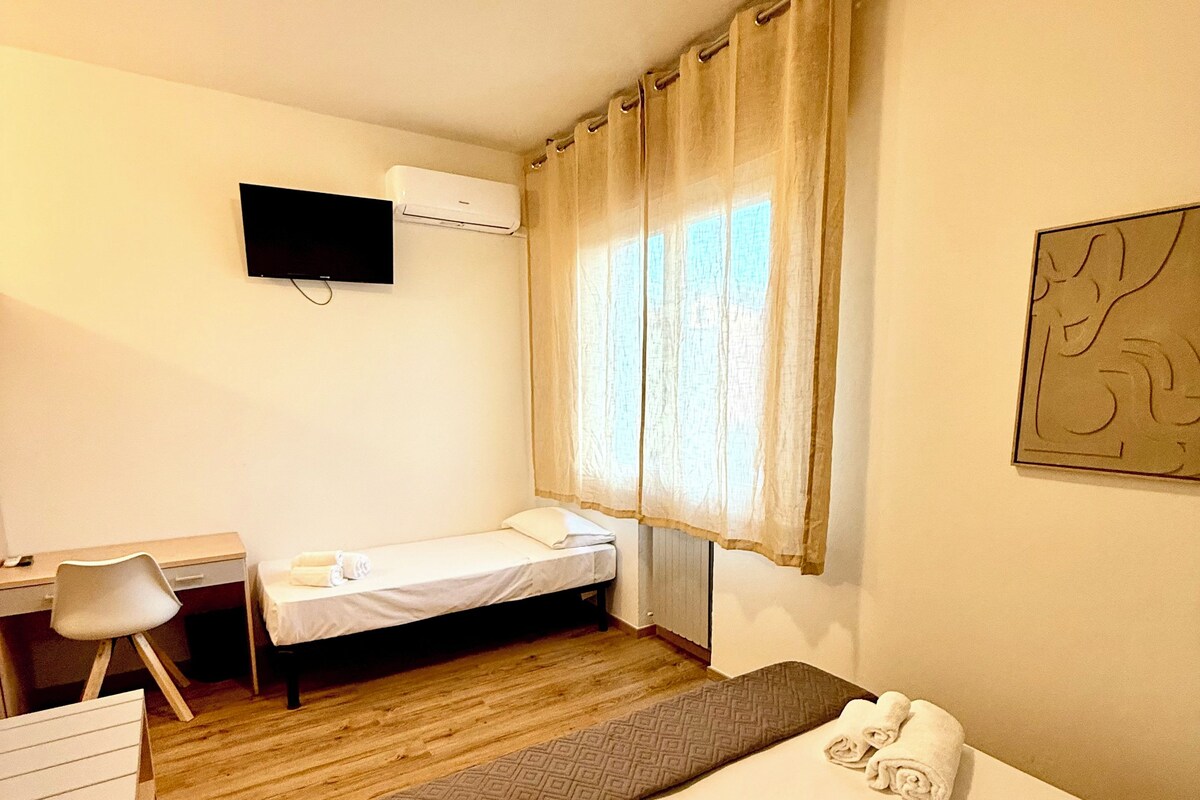 A hotel room with a bed, a desk, a chair, a TV, and a window with curtains.